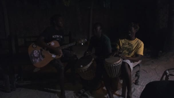 Jóvenes africanos locales tocan la guitarra con djembe, cantan canciones alrededor de fogata, noche — Vídeos de Stock