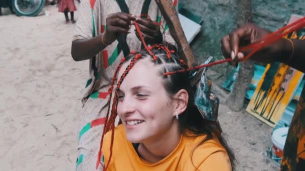 Mujer africana tejiendo trenzas africanas con Kanekalon rojo al aire libre, Zanzíbar África — Vídeo de stock