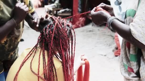 Процесс плетения африканских кос с красным Kanekalon на открытом воздухе, Занзибар, Африка — стоковое видео