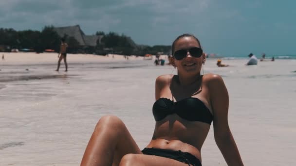 Jeune femme en bikini noir bronzage sur une plage de sable blanc Paradise se trouve près de l'océan — Video