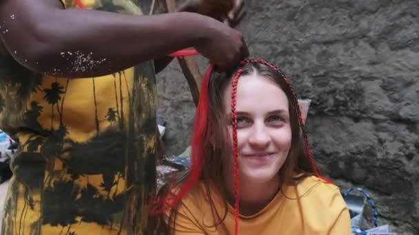 Proceso de tejer trenzas africanas con Kanekalon rojo al aire libre, Zanzíbar, África — Vídeo de stock