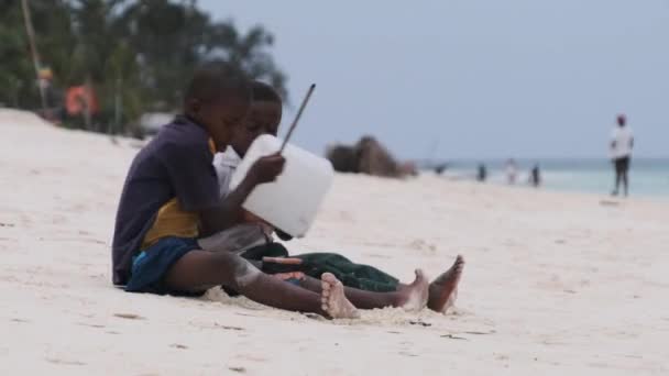 Δύο ντόπια αγόρια της Αφρικής κάθονται στην παραλία και παίζουν αυτοσχέδια τύμπανα μπουκαλιών, Zanzibar — Αρχείο Βίντεο