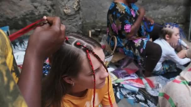 Αφρικανική γυναίκα υφαίνοντας αφρικανικές πλεξούδες με κόκκινο Kanekalon Εξωτερική, Ζανζιβάρη Αφρική — Αρχείο Βίντεο