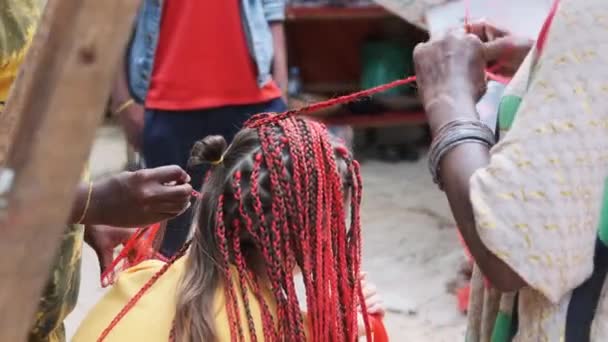 Mulher Africana tecendo tranças africanas com Kanekalon vermelho ao ar livre, Zanzibar África — Vídeo de Stock