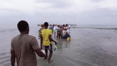 Bir grup turist, Afrika 'daki bir tekneye binmek için sığ sularda yürüyor.