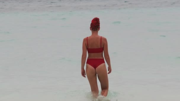 Mladá žena v červených plavkách vejde do tyrkysového oceánu na pláži Paradise