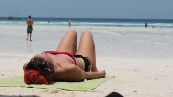 Ung kvinna solar på en sandstrand i paradiset liggandes i röd bikini nära havet — Stockvideo