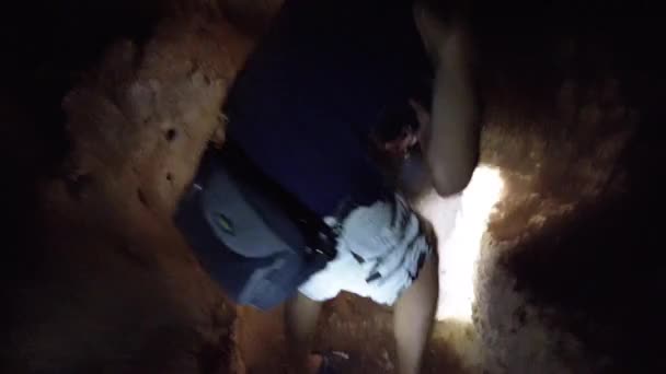 L'homme explore les stalactites à l'intérieur d'une grotte sombre profonde, éclairant avec une lampe de poche — Video