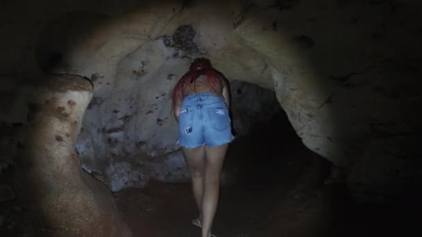 Mulher explora estalactites dentro de uma caverna escura profunda, iluminando com lanterna — Vídeo de Stock