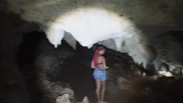 Mulher explora estalactites dentro de uma caverna escura profunda, iluminando com lanterna — Vídeo de Stock