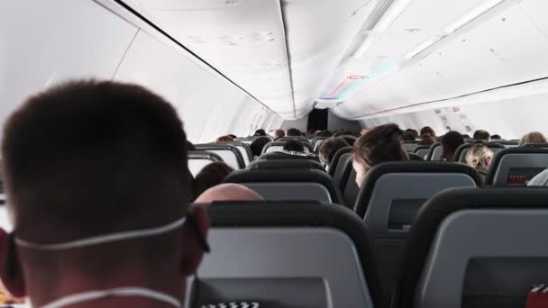 Кабина пассажирского самолета с людьми в масках, сидящими в креслах во время полета — стоковое видео