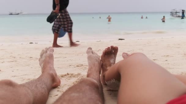 海によって熱帯の砂浜に横たわっている男性と女性のカップルのPOV足 — ストック動画
