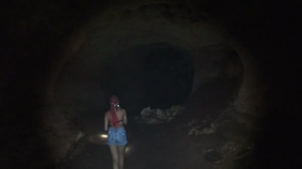 Donna esplora stalattiti all'interno di una profonda grotta oscura, illuminante con torcia elettrica — Video Stock