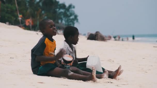 Dois meninos africanos locais sentam-se na praia e tocam tambores de garrafa improvisados, Zanzibar — Vídeo de Stock