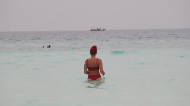 Kırmızı mayo giymiş genç bir kadın Cennet Sahili 'ndeki Turkuaz Okyanusu' na giriyor. — Stok video