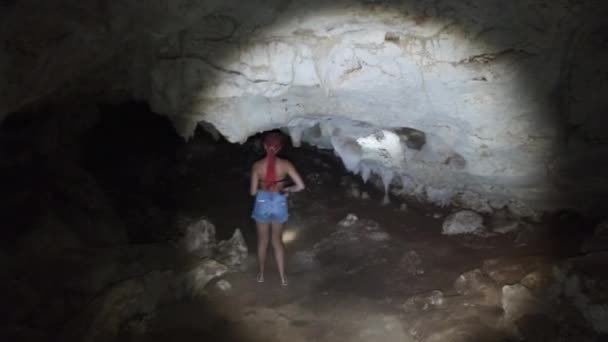 Kobieta odkrywa Stalaktyty w głębokiej ciemnej jaskini, oświetlając je latarką — Wideo stockowe
