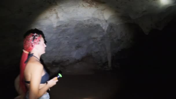 Vrouw onderzoekt stalactieten in een diepe donkere grot, verhelderend met zaklamp — Stockvideo