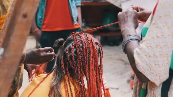Afrikaanse vrouw weven Afrikaanse vlechten met rode Kanekalon Outdoor, Zanzibar Afrika — Stockvideo