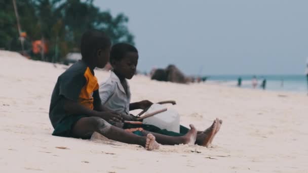 Zwei lokale afrikanische Jungen sitzen am Strand und spielen improvisierte Flaschentrommeln, Sansibar — Stockvideo