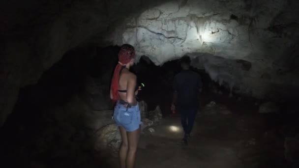Женщина исследует сталактитов в глубокой темной пещере, освещенной фонариком — стоковое видео