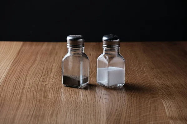 Cam şişelerdeki tuz ve biber bir restoranın ahşap masasında duruyor.