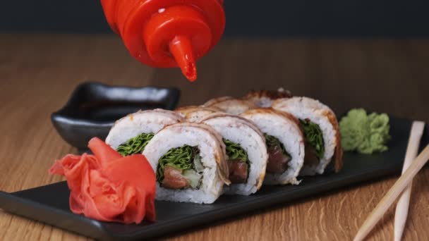 Apetyczne sushi polewa się słodkim sosem na drewnianym stole w restauracji — Wideo stockowe