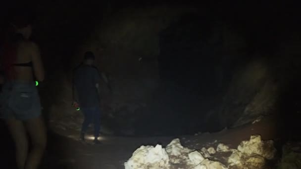 Mujer explora las estalactitas dentro de una cueva oscura profunda, iluminando con linterna — Vídeo de stock