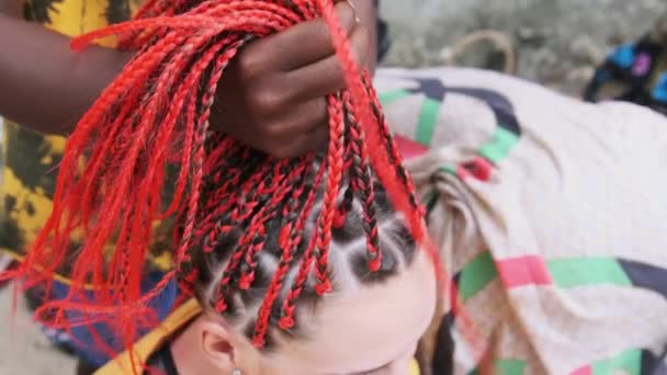 Femme africaine tissant des tresses africaines avec Kanekalon rouge en plein air, Zanzibar Afrique — Video