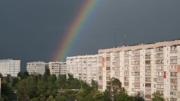 Огромная радуга в облачном небе над домами в городе — стоковое видео