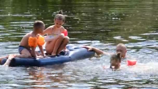 Τα παιδιά κολυμπούν και παίζουν σε ένα Φουσκωτό στρώμα στον ποταμό σε ζεστή καλοκαιρινή μέρα — Αρχείο Βίντεο