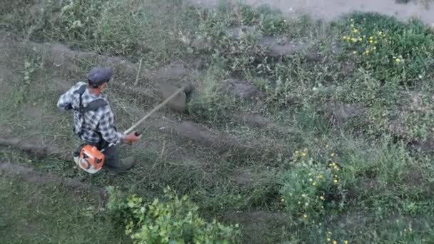 Homem corta a grama com um cortador de grama a gasolina manual — Vídeo de Stock