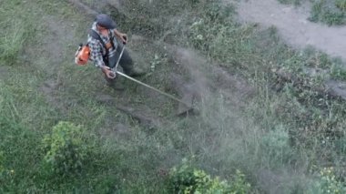 Adam, çimleri elle biçme makinesiyle biçiyor.