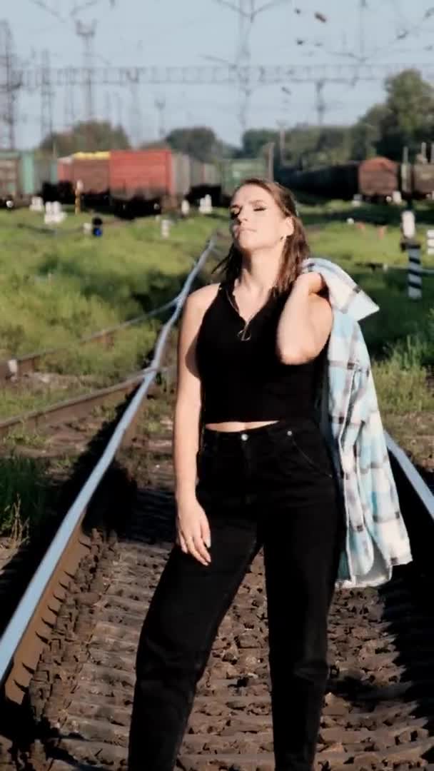 Вертикальна, молода сексуальна жінка стоїть на поїзді треки і дивиться на камеру . — стокове відео