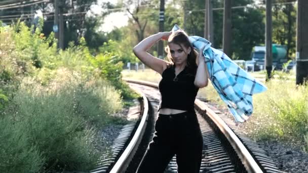 Joven mujer sexy se para en las vías del tren y mira a la cámara. — Vídeos de Stock