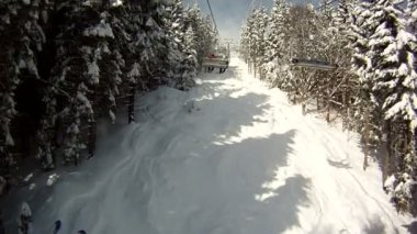 Kayakçı kayak teleferiği üzerinde yükselir. Panorama ve dağlar, ağaçlar karla kaplı manzara çevresinde. Teleferik göster.
