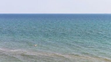 Bir adam bir ıssız plajda denizde yüzüyor.