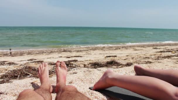 As pernas de duas pessoas são banhos de sol na praia junto ao mar . — Vídeo de Stock