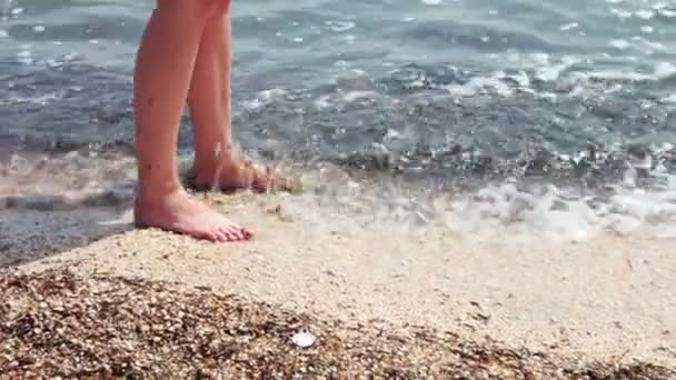 Jambes d'une belle fille sur une plage de sable lavée par les vagues de la mer . — Video