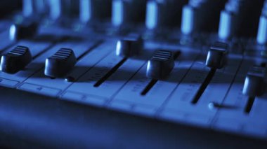 Sabit ses karıştırıcı faderlerin makro yakın çekim görüntüleri, detaylı doku ve kanal işaretlerini dramatik, değişken mor, mavi ve turuncu Bokeh ışıkları ile karanlık, atmosferik bir stüdyoda gösteriyor..