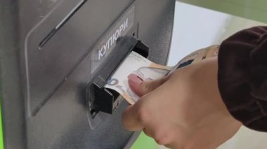 Yan açılı yakın plan insanlar kahverengi kollu Ukrayna Hryvnia banknotunu Ukrayna 'daki bir elektronik ödeme işlemini gerçekleştiren bir self-servis büfesinin nakit alıcısına yerleştiriyorlar..