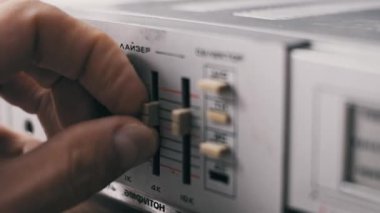 Eski gümüş stereo ekipmanların ses frekanslarını, Kiril alfabetik metin ve sığ alan derinliği ile ayarlayan bej kaydırıcıları klasik grafik dengeleyicisine ayarlayan parmakların yakın plan çekimi..