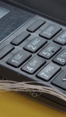 Aşırı yakın plan, siyah ödeme terminalinin makro görüntüsü sayısal tuş takımı. Detaylı görünüm, rakamların ve harflerin bulunduğu düğmelerin dokusunu gösterir. Taşınabilir veya sosyal medya kullanımı için dikey biçim.