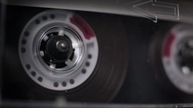 Şeffaf bir kasetin kapak makrosu güvertede oynanıyor, kusursuz bir döngü yaratıyor. Lekeli delikleri olan beyaz makarası, karanlık manyetik film dağıldıkça sürekli döner..