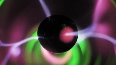 Pembe ve mor elektrik cıvataları yayan merkezi siyah elektrotlu yakın çekim plazma topu. Dönen iyonize gaz lifleri yeşil bir parıltıyla cam küre içinde hareket eder..