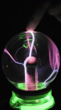 Yakından bakınca insan parmağı cam küre yüzeyine değiyor. Pembe beyaz elektrik telleri temas noktasını takip ediyor. Merkezi elektrot iyonize gaz filizleri yayar. Yeşil parlayan taban, koyu arkaplanı aydınlatıyor.