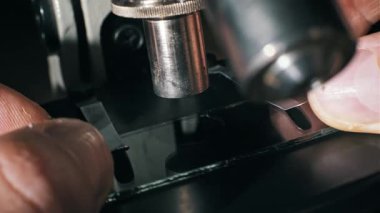 Yan açı, mikroskop sahnesine cam bir kaydırak yerleştiren parmaklar. Bir pipet temiz bir ayıraç damlası ekler, ve başka bir cam plaka numuneyi kaplar, laboratuvar çalışması için ıslak bir tepe hazırlar..