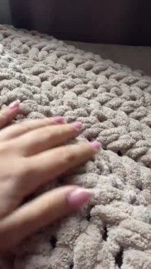 Fransız manikürlü, dikey, yakın plan bir kadın eli yumuşak, bej renkli, tıknaz bir battaniyeyi nazikçe okşuyor. Parmakları, rahat ve rahatlatıcı kumaşın yumuşacık dokusunu hisseder..