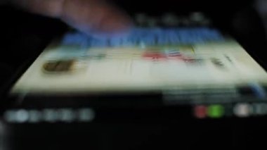 Düşük açılı makro bir parmak görüntüsü sosyal medyayı karanlık bir odada akıllı telefon ekranında hızla kaydırıyor. Hareket, gece veri akışı ve dijital tüketimi gösteren metin ve görüntüleri bulanıklaştırır.