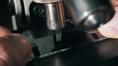 Metal klipslerin mikroskop sahnesine cam bir kayma yerleştirdiği makro görüntü. Bir pipet daha sonra bilimsel analiz için temiz bir sıvı damla ekler veya karanlık bir odada bir laboratuvar deneyi.