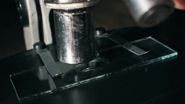 Vintage bir mikroskop, cam bir kaydırağın üzerine metal objektif lensleri kapatır. Bir pipet, bilimsel bir deneyde ya da laboratuvar araştırmasında örnek hazırlamak için koyu arkaplan içeren temiz sıvıyı damlatır..